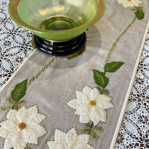 Carried Away Designs linen-colored table runner with three white poinsettia flowers at each end over white lace tablecloth with green vintage bowl