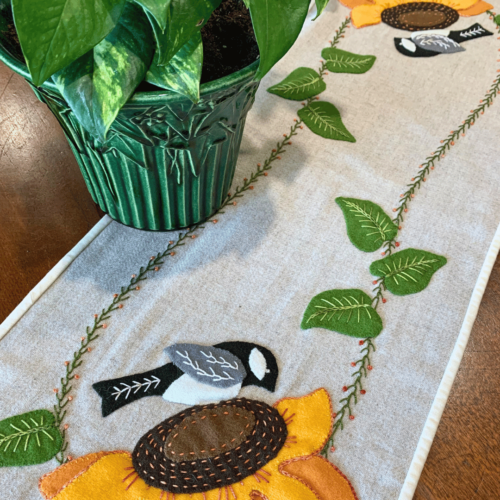 Carried Away Designs linen-colored table runner with two chickadee on sunflower at each end with plant in center