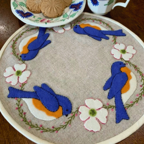 Carried Away Designs linen-colored round table mat with bluebirds and white flowers
